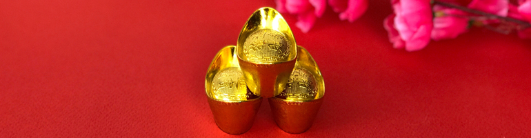 Three gold pendants are towered in a triangle on a red background with cherry blossoms in the background. This represents the trines in the Chinese zodiac.